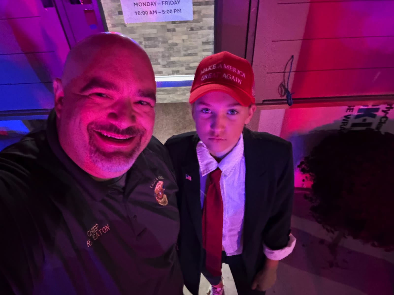 Chief R. Eaton selfie with a youth in a red necktie and red hat under pink and purple event lighting