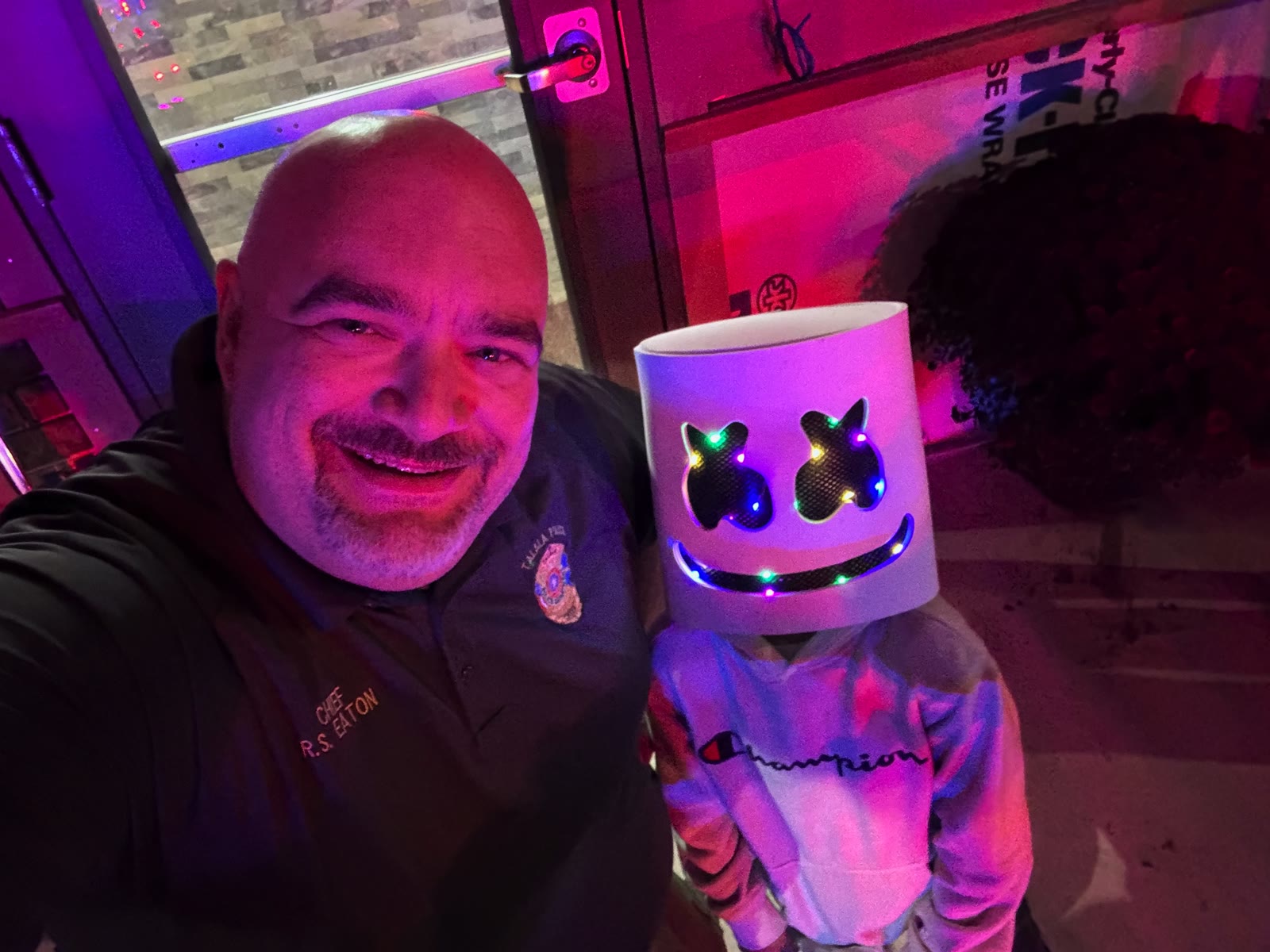 Chief R. Eaton selfie with a child wearing a light-up Marshmello mask under purple event lighting