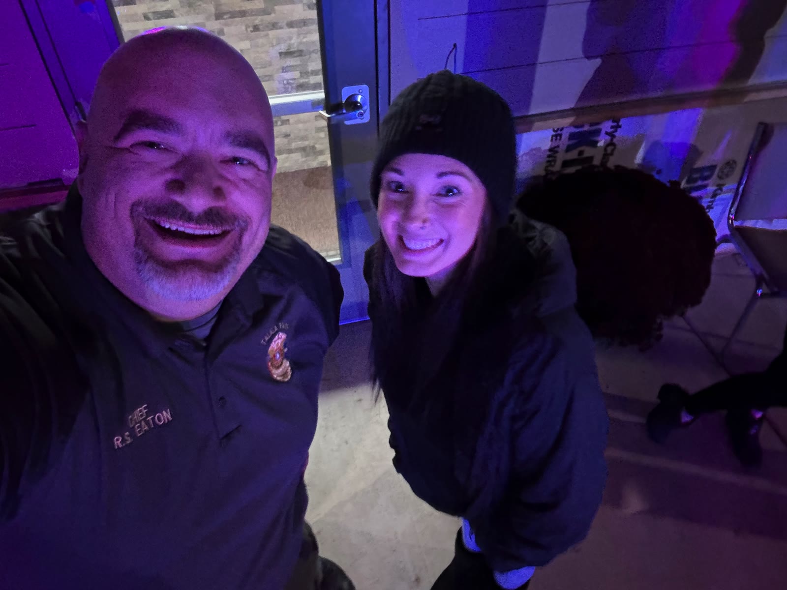 Chief R. Eaton selfie with a smiling young woman in a black beanie under purple event lighting