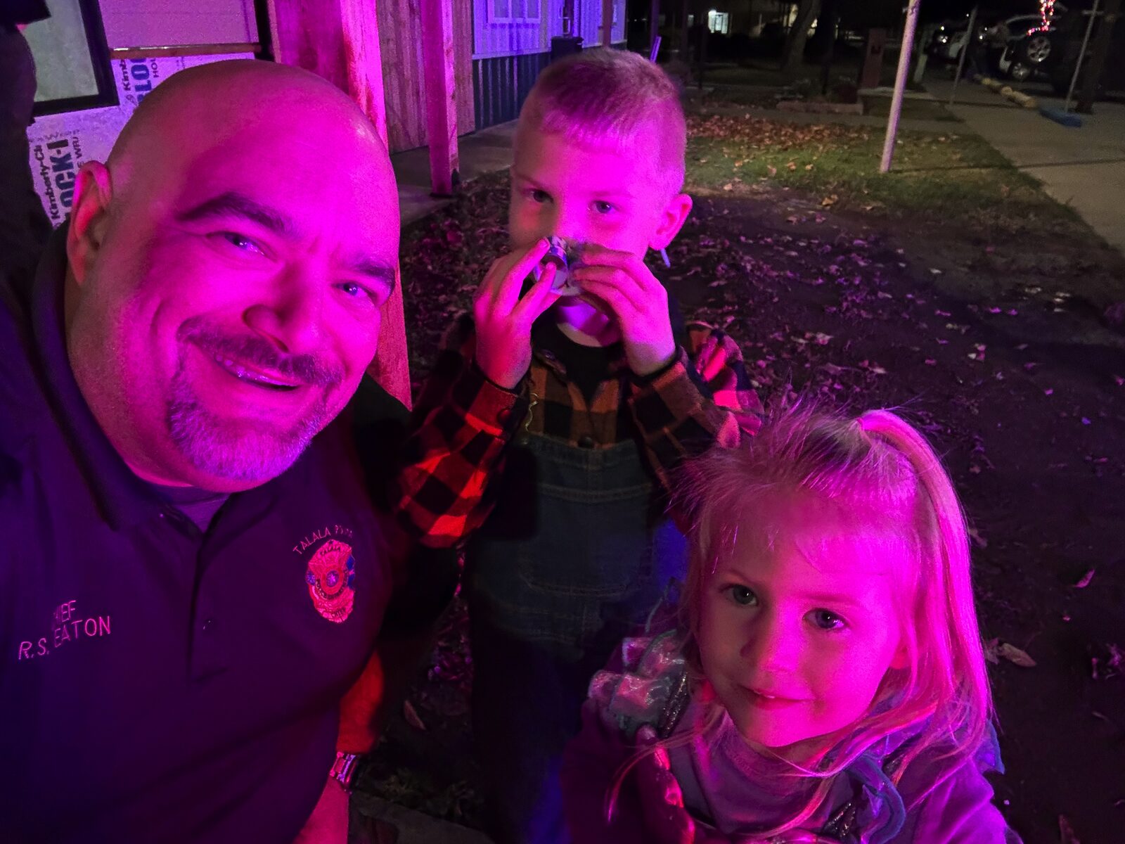 Chief R.S. Eaton selfie with two young community members under bright pink event lighting; Chief embroidery visible on his polo