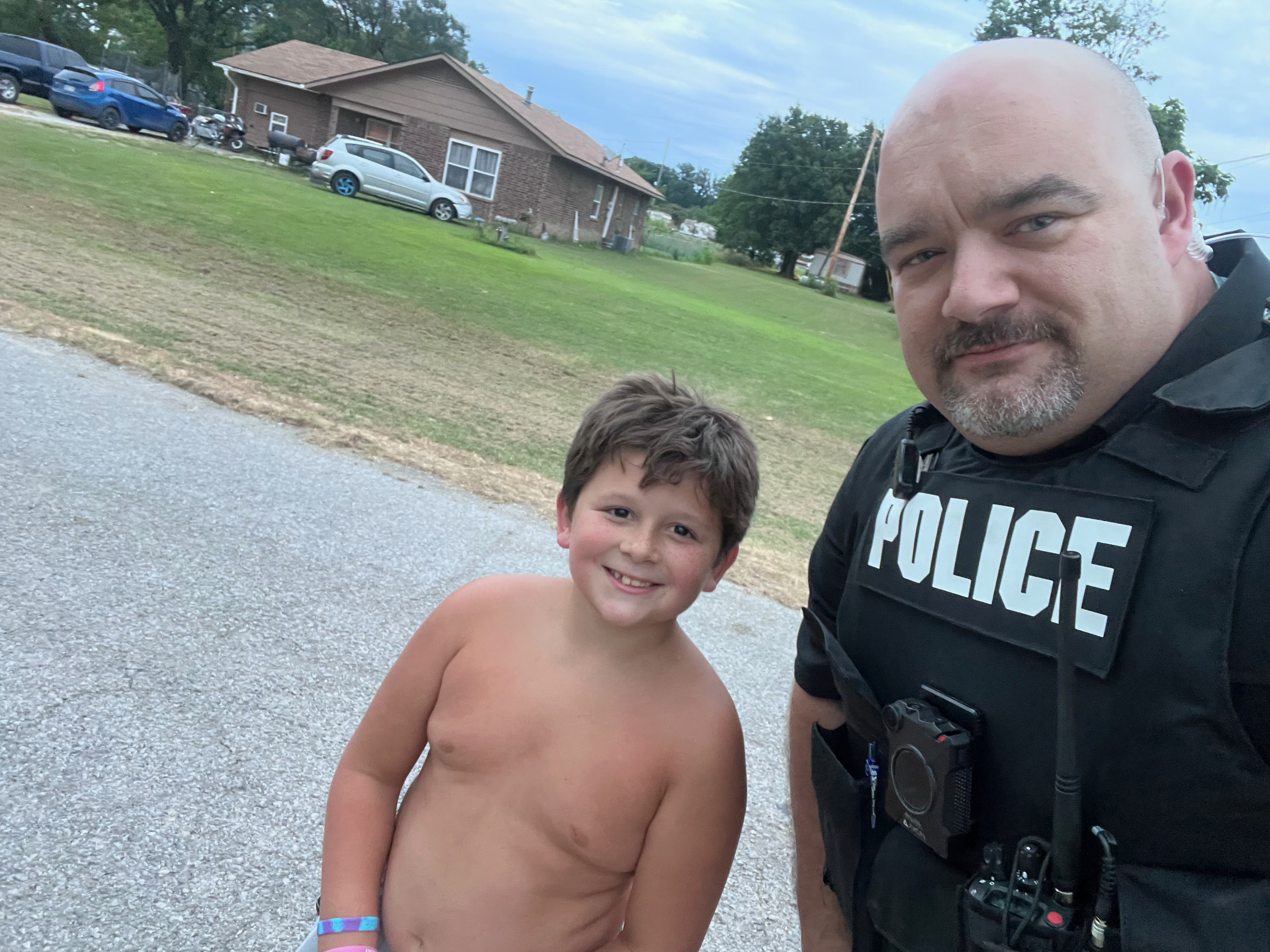 Talala Police officer in a POLICE vest with a smiling local youth outdoors